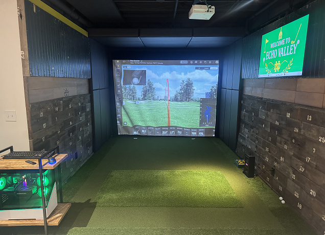 Indoor golf simulator with wood paneled walls.