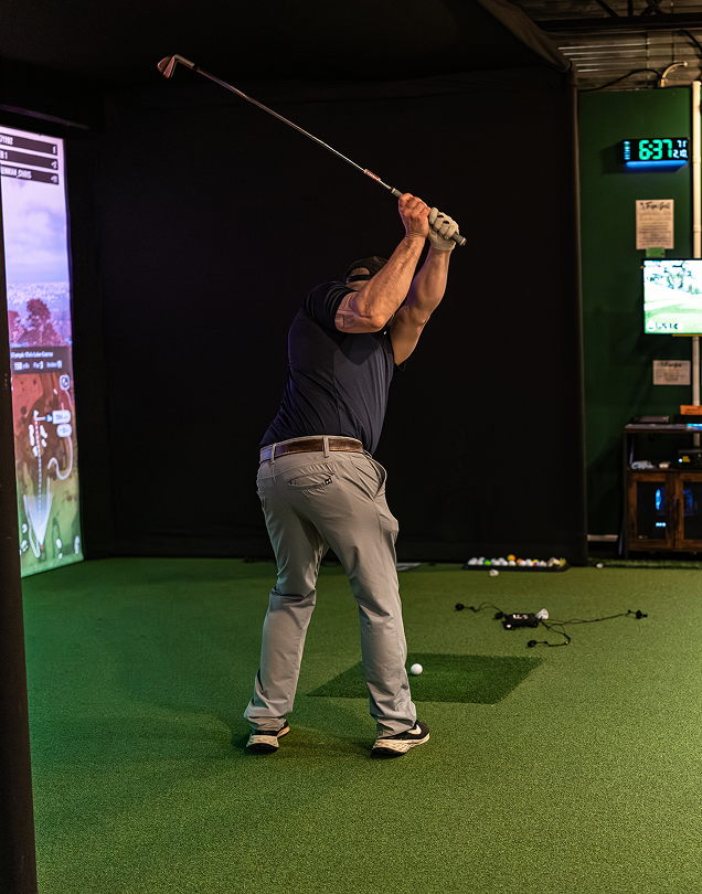 Golfer swinging a club in an indoor simulator.
