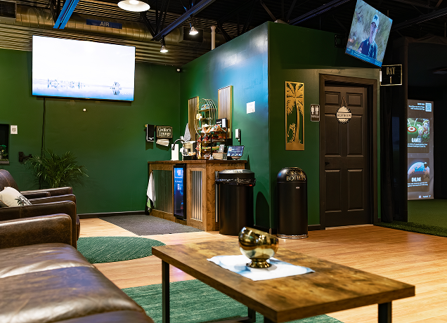 Indoor golf lounge with a bar and seating.