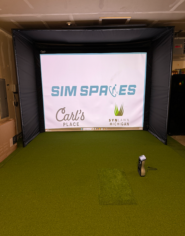 Fully assembled golf simulator enclosure displaying sponsor logos on the screen