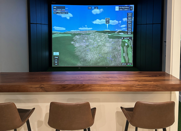 Wooden bar overlooking an indoor golf simulator screen.
