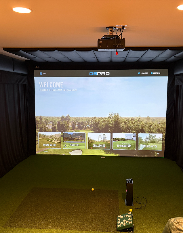 Indoor golf simulator setup displaying the GSPro welcome screen on a large projection screen.