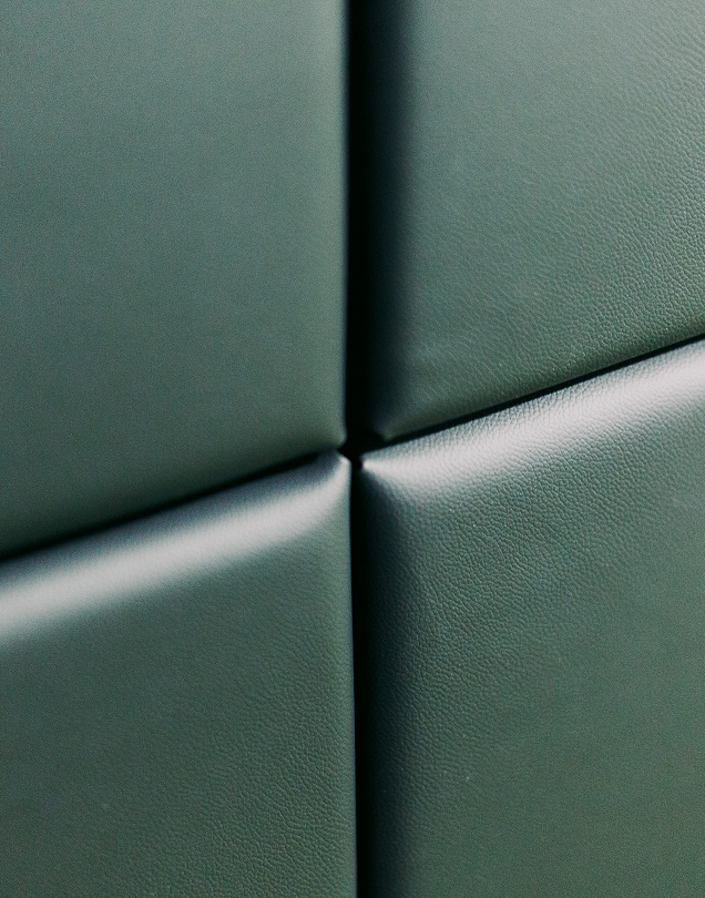 Close-up texture of dark green padded leather wall panels.